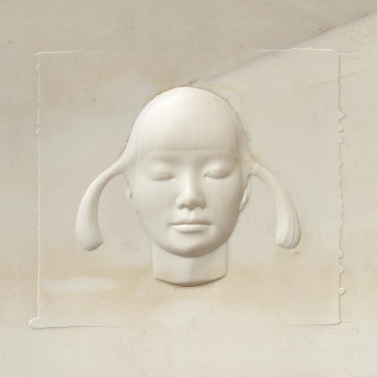 White sculpture of a face with pigtails on a beige background